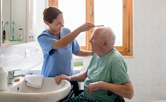caregiver helps elderly man brush his hair
