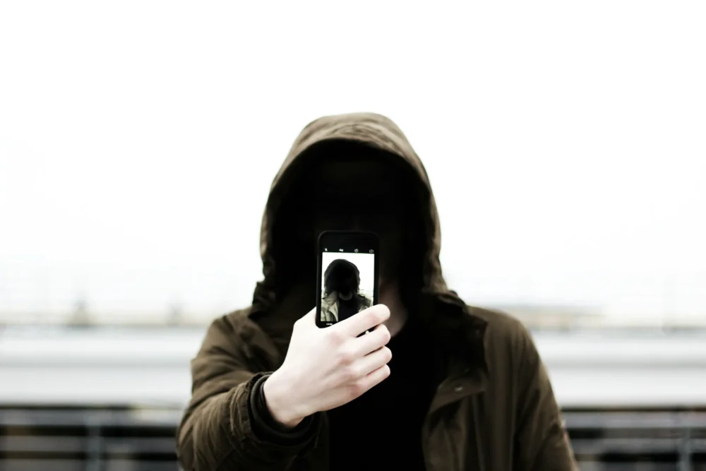 Hooded person holding a phone over their face: Photo by Tom Sodoge on Unsplash
