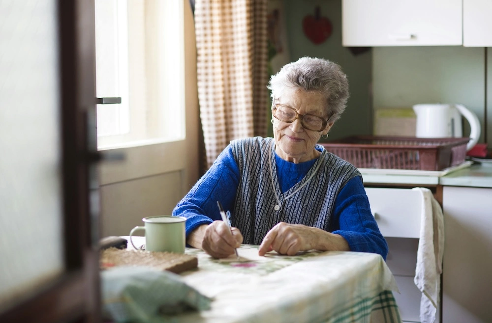 senior woman sitting at table smiling and writing